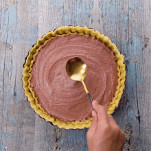 a person is using a gold spoon to fill a pie with chocolate filling