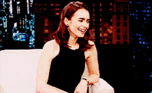 a woman in a black dress is sitting on a couch smiling