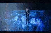 a man in a suit stands on a stage holding a microphone in front of a screen that says poland
