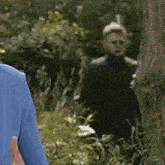 a man in a blue shirt is standing next to a woman in a black jacket in the woods .