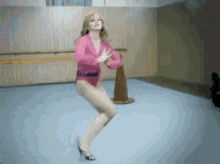 a woman in a pink leotard and high heels is dancing on a blue floor .