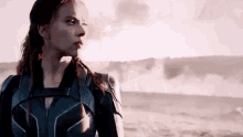 a woman in a black suit is standing in the middle of a desert looking at the camera .