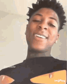 a young man wearing a black t-shirt with a yellow eye on it is smiling and looking at the camera .