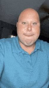 a bald man is wearing a blue shirt and making a funny face