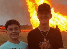 a man and a boy are posing for a picture in front of a large fire .