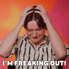 a man in a striped shirt has his hands on his head and the words i 'm freaking out above him