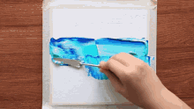 a person is using a spatula to spread blue paint on a white piece of paper