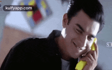 a man is smiling while talking on a yellow cell phone .