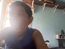 a young boy in a blue tank top is looking at the camera