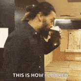 a man in a black shirt is drinking from a cup while standing in a kitchen .