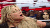 a woman is standing in a wrestling ring with her mouth open and her hair blowing in the wind .