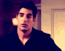 a man in a black shirt is standing in front of a door looking at the camera .