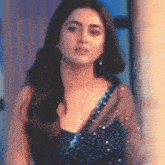 a woman in a blue dress is standing in front of a window looking at the camera .