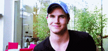 a man wearing a baseball cap and a black shirt smiles