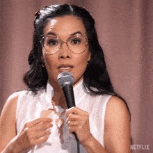 a woman wearing glasses is holding a microphone in front of a netflix logo .