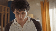 a young man with curly hair is wearing a white shirt and a black sweater