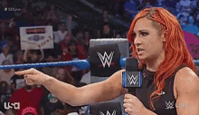 a woman with red hair is holding a microphone and pointing at something .