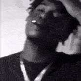 a man is smoking a cigarette in a black and white photo while wearing a necklace .
