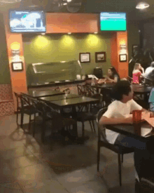 a man sits at a table in a restaurant with a tv above him