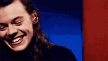 harry styles is smiling with his eyes closed in front of a blue and red background .