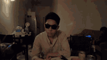 a man wearing sunglasses in a dark room with a bottle of aquafina water behind him
