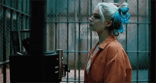 harley quinn is standing in a prison cell with a blue ribbon in her hair .
