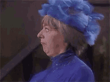 a woman wearing a blue hat and a purple dress is making a funny face