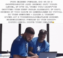 two men are sitting at a table with a laptop and one of them is wearing a blue shirt