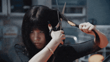 a woman is cutting her hair with scissors while wearing a bracelet