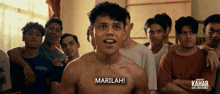 a shirtless man stands in front of a group of men and says marilah