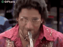 a man in a pink shirt is playing a saxophone while wearing glasses .