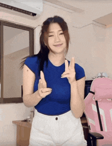a woman wearing a blue shirt and white shorts is giving the peace sign