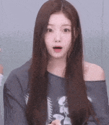 a girl with long hair is wearing a gray off the shoulder sweater and making a surprised face .