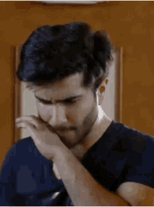 a man with a beard is covering his mouth with his hand and looking down .