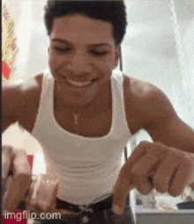 a man wearing a white tank top is smiling and pointing at something .