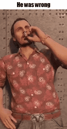a man in a paisley shirt is smoking a cigarette while standing in front of a metal wall .
