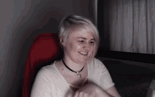 a woman wearing a necklace and a white shirt smiles