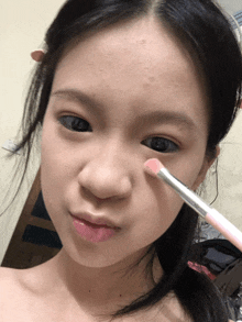a woman is applying makeup to her face with a brush