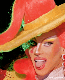 a drag queen is sticking her tongue out while wearing a large hat