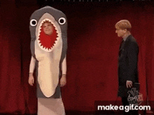 a man in a suit is standing next to a man in a shark costume .