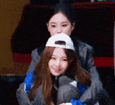 two girls are sitting next to each other with one wearing a baseball cap .