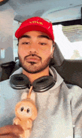 a man wearing a red vitar hat is holding a stuffed animal