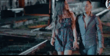 a man and a woman are holding hands while walking on a train track .