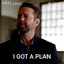 a man with a beard is standing in front of a window and says i got a plan
