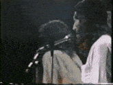 a man with long hair is singing into a microphone while playing a keyboard on a stage .