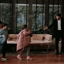 a little girl in a pink coat is playing with a teddy bear in a living room