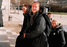 a group of people are walking down stairs and one of them is wearing a black jacket with a green badge on the back