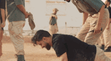 a man in a black shirt is kneeling on the ground while another man stands behind him