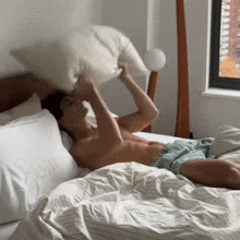 a shirtless man laying on a bed holding a pillow over his head