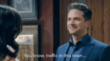 a man in a suit talks to a woman in a room and says " you know traffic in this town "
